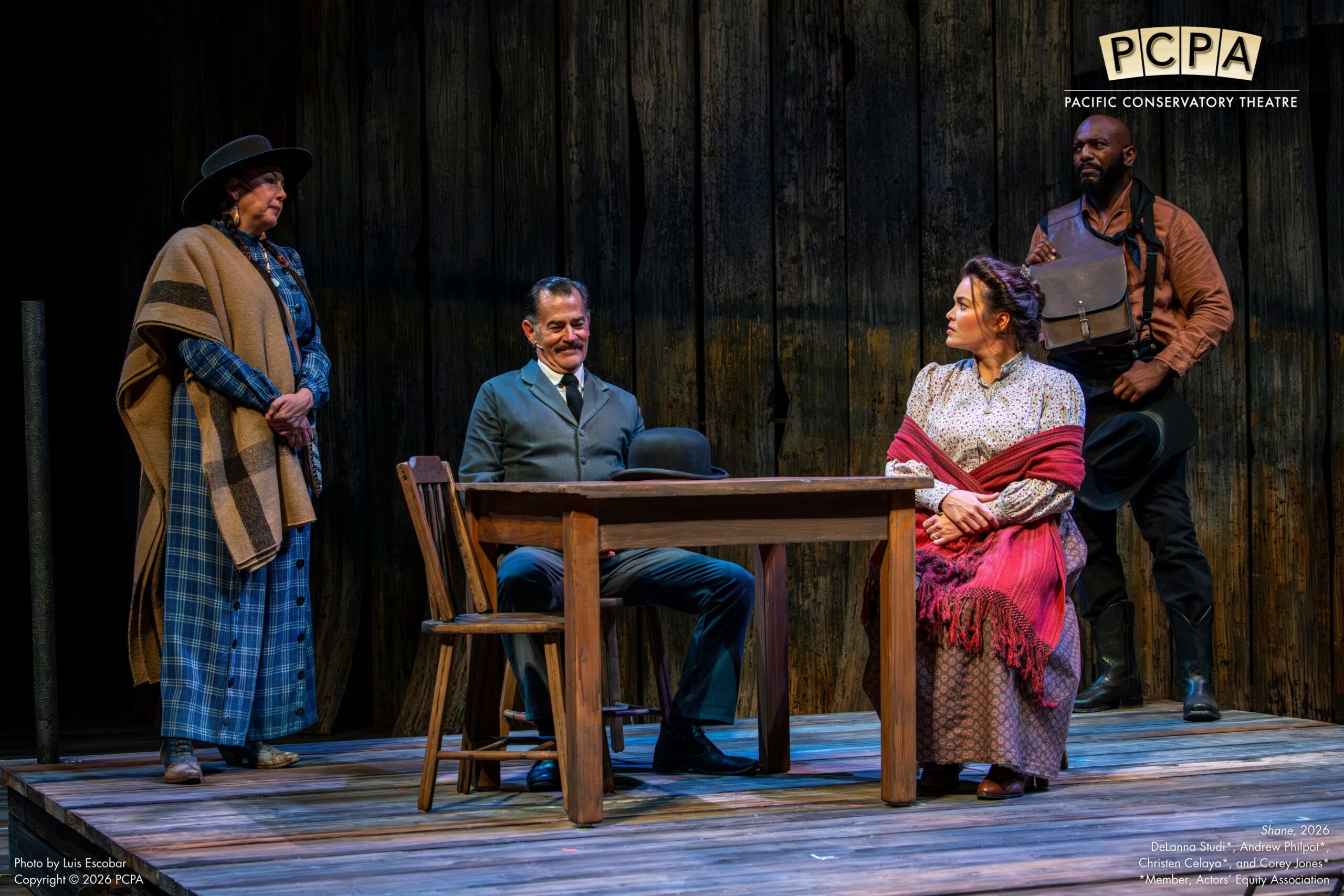 Man and woman sitting on stage while two others stand around the table