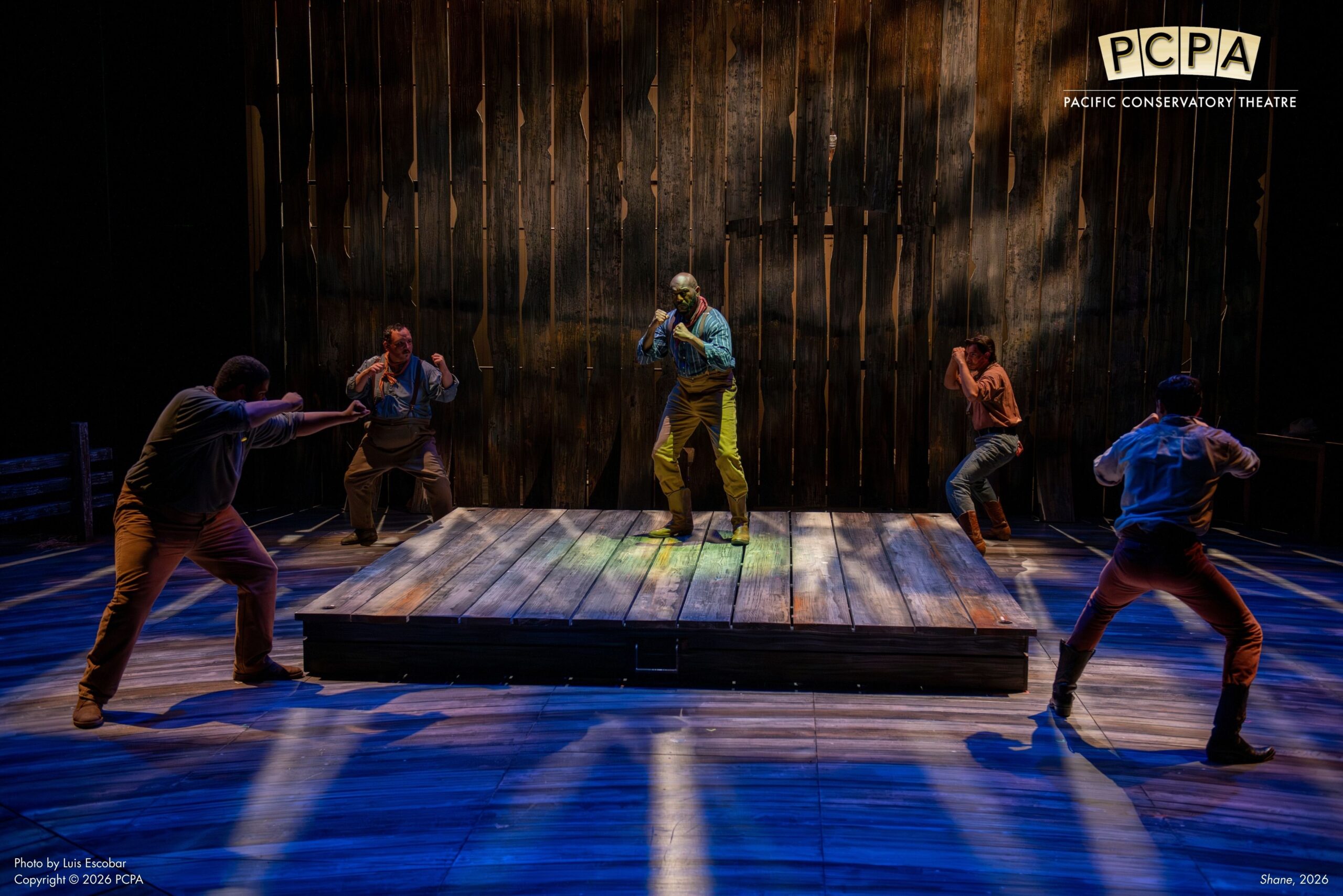 Ensemble cast on stage standing with fist up in circle