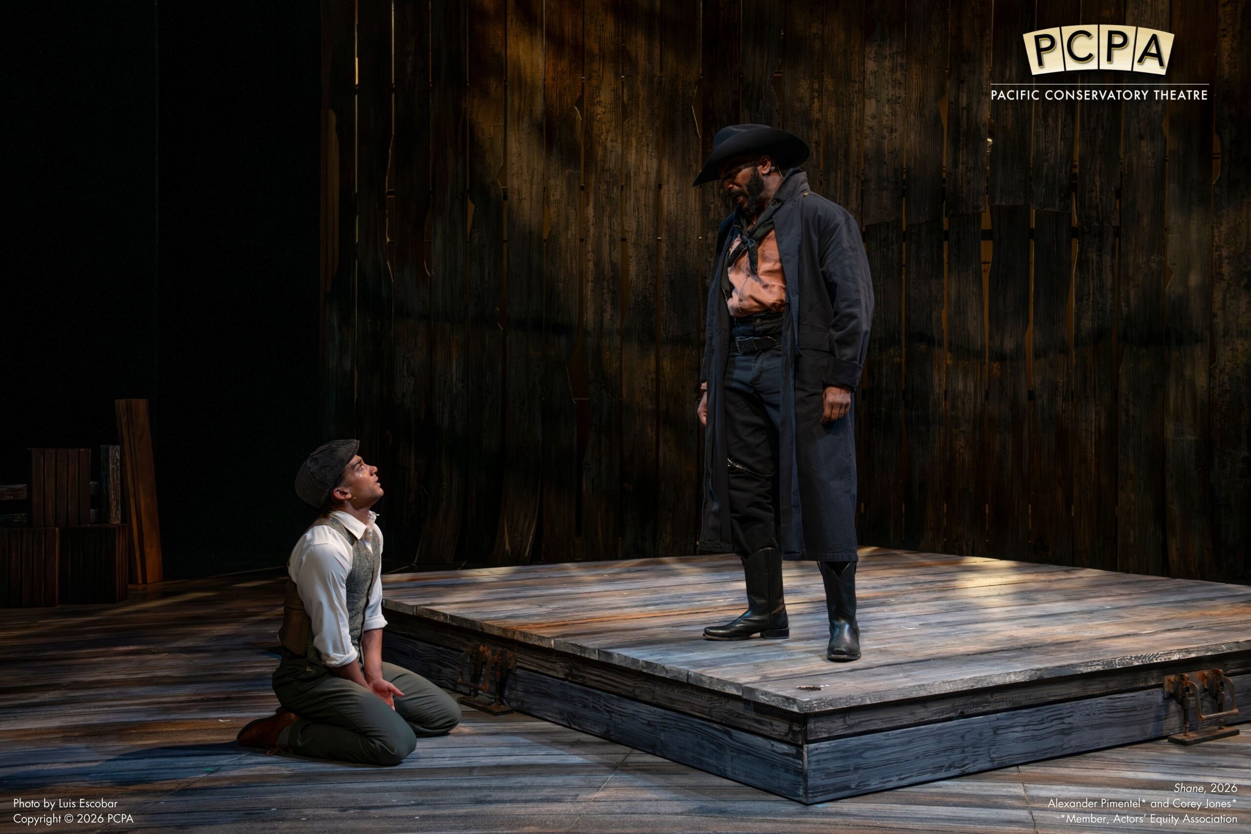 Actor standing on platform while other actor is looking up at him while sitting on knees